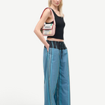 A person wearing a black tank top and Mateo Pant trousers with vertical blue stripes and a dark drawstring waistband, carrying a small, embroidered shoulder bag.