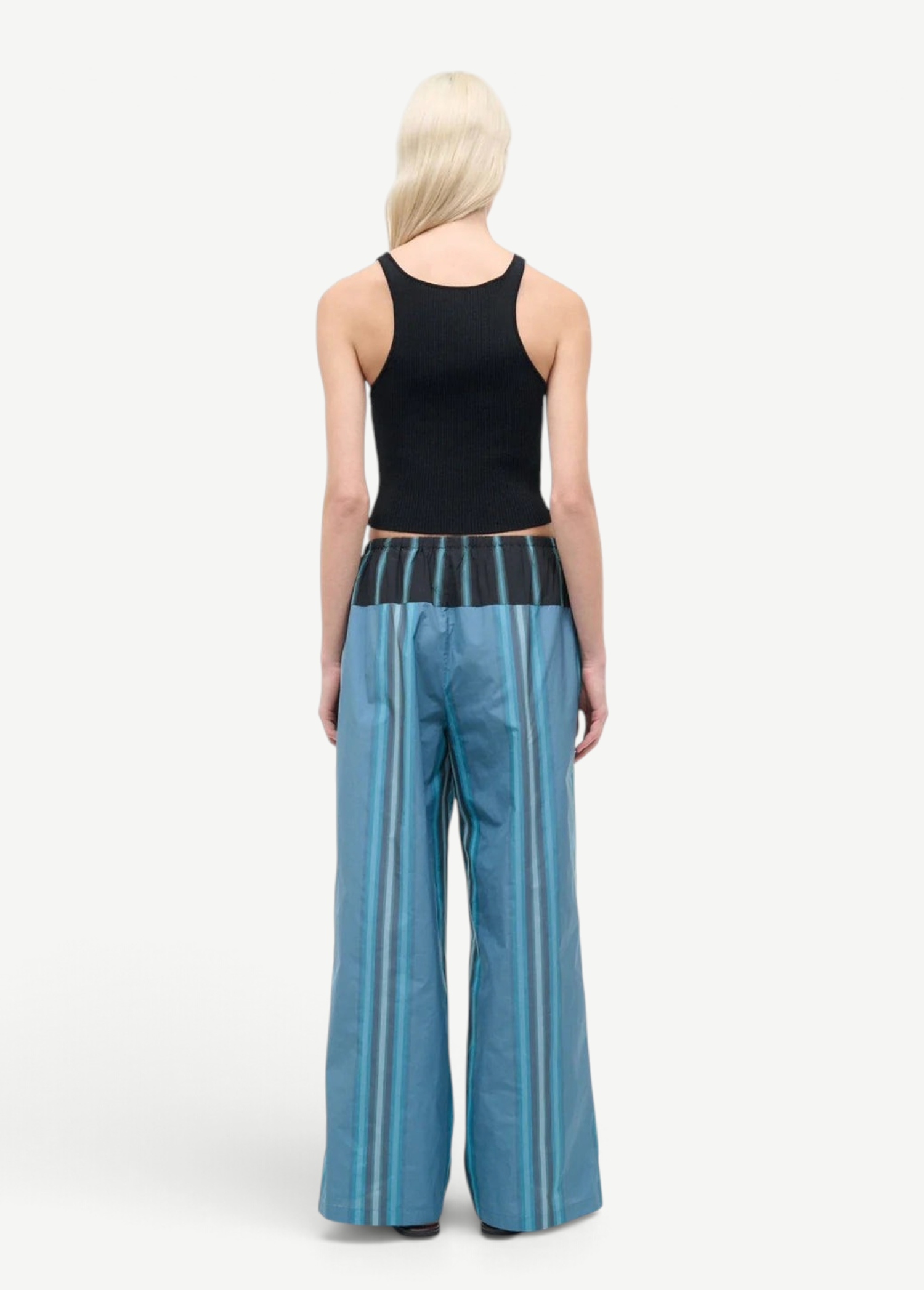 A person seen from behind wears a black ribbed tank top and Mateo Pant wide-leg trousers, featuring blue vertical stripes and a dark contrasting waistband.