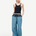 A person wears a black ribbed tank top and Mateo Pant, featuring blue striped fabric and a black drawstring waistband.