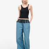 A person wears a black ribbed tank top and Mateo Pant, featuring blue striped fabric and a black drawstring waistband.