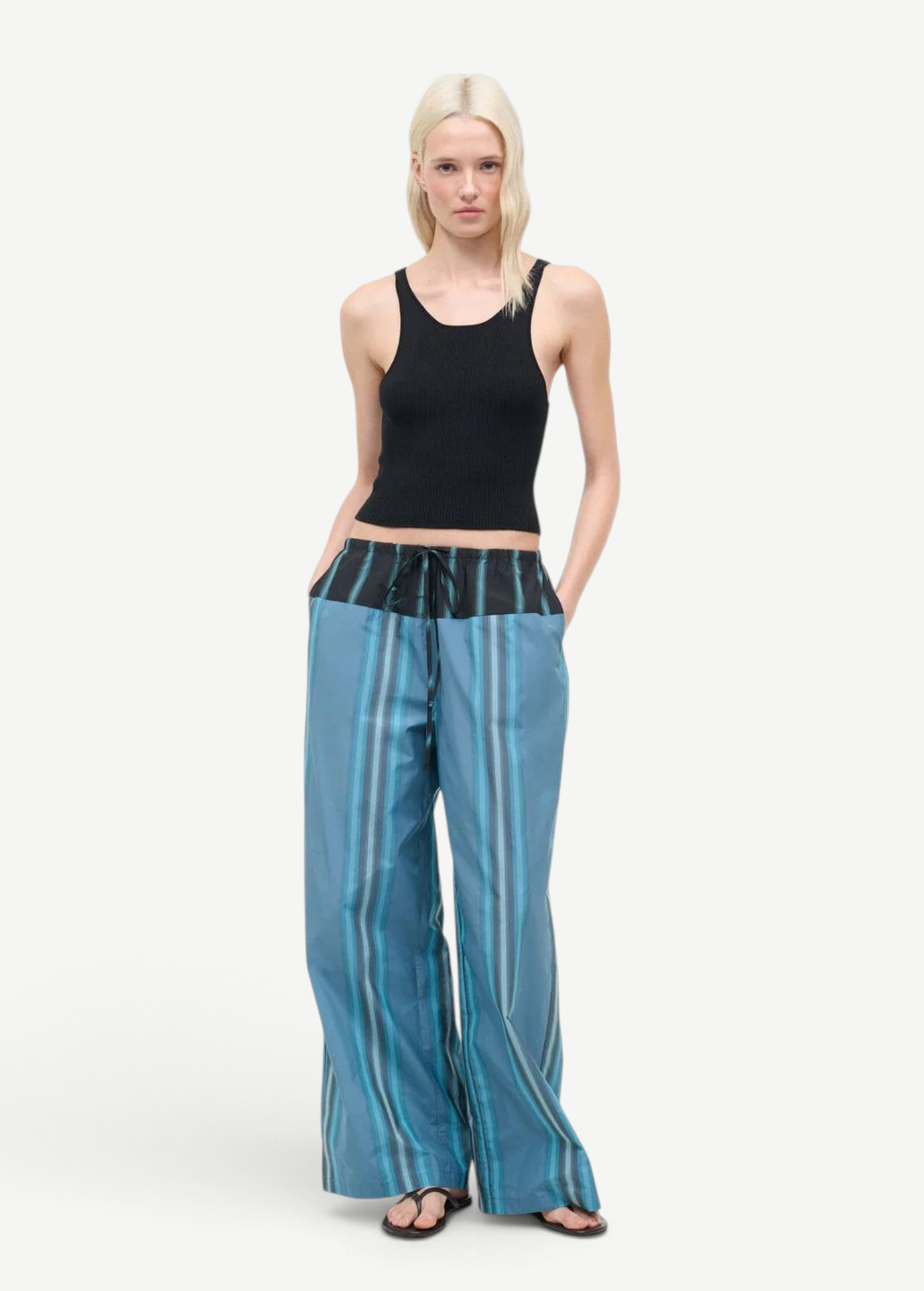 A person wears a black ribbed tank top and Mateo Pant, featuring blue striped fabric and a black drawstring waistband.