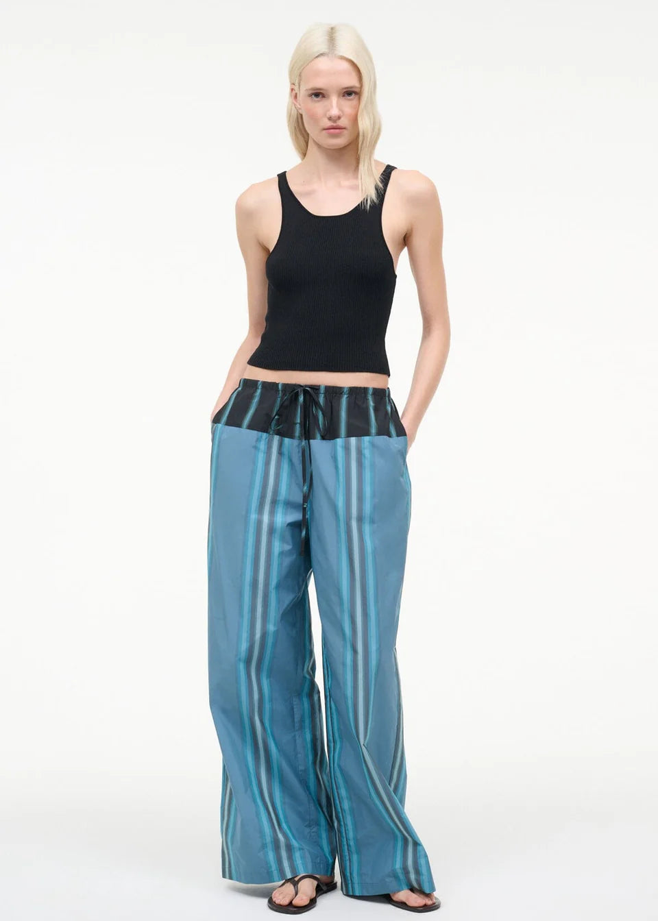 A person wears a black ribbed tank top and Mateo Pant, featuring blue striped fabric and a black drawstring waistband.