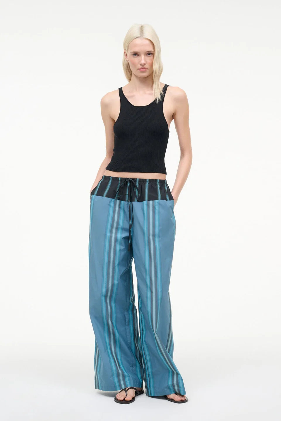 A person wears a black ribbed tank top and Mateo Pant, featuring blue striped fabric and a black drawstring waistband.