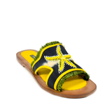 Introducing the Mazu Slide: these hand-embroidered leather sandals feature a brown sole, yellow footbed, and a black strap adorned with a yellow beaded starfish and green fringe accents—making them a stunning example of sustainable footwear.