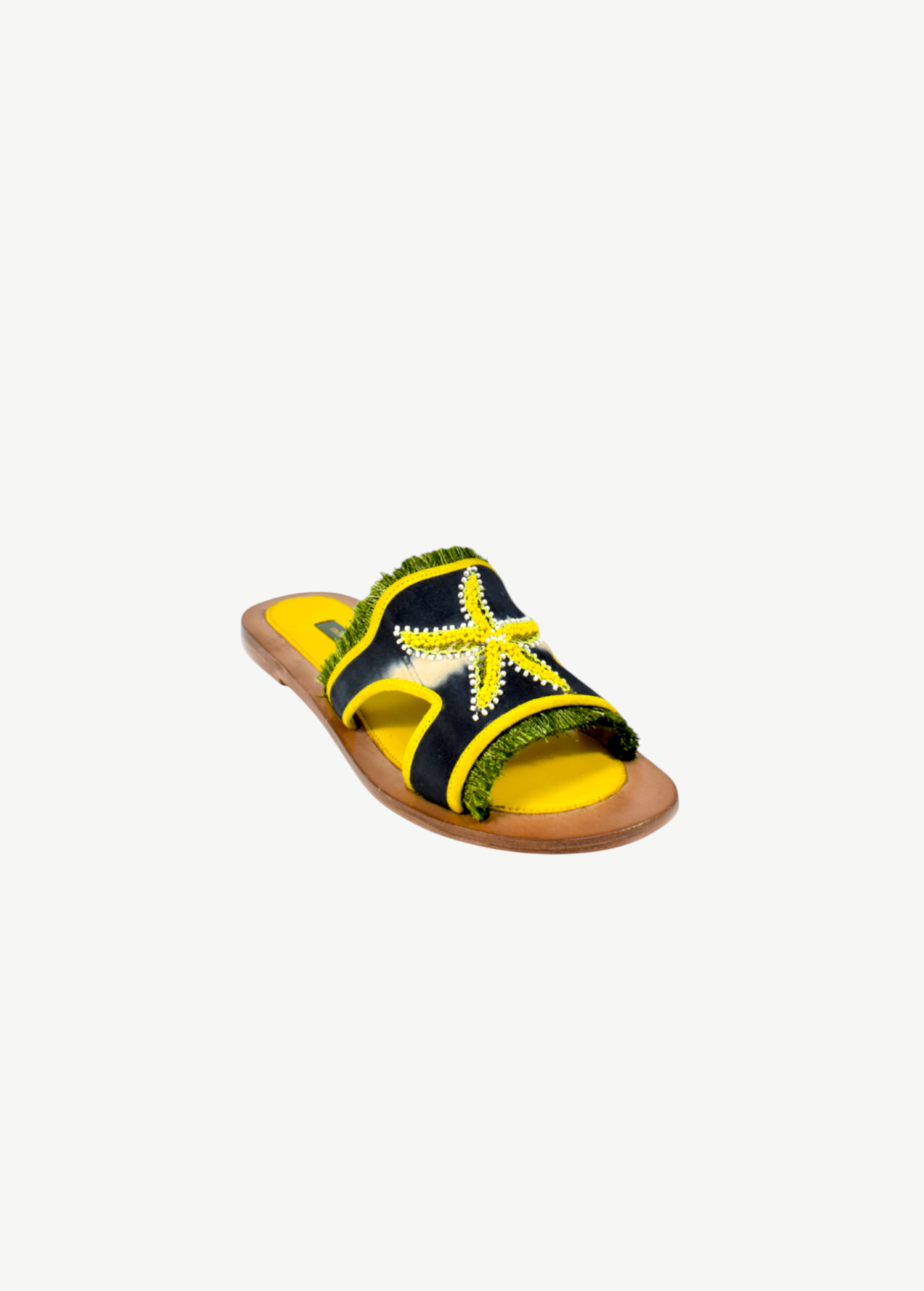 Introducing the Mazu Slide: these hand-embroidered leather sandals feature a brown sole, yellow footbed, and a black strap adorned with a yellow beaded starfish and green fringe accents—making them a stunning example of sustainable footwear.
