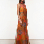 The Albee Dress is an elegant, floor-length gown in sheer orange fabric featuring a colorful, oversized floral print, a sleeveless design, and a high-neck silhouette.