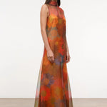 The Albee Dress is an elegant, floor-length gown in sheer orange fabric featuring a colorful, oversized floral print, a sleeveless design, and a high-neck silhouette.
