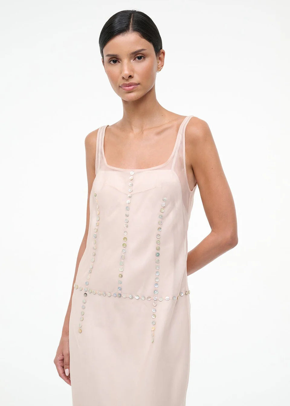 The Greta Dress is an elegant, sleeveless light pink midi dress with a square neckline and rows of small, iridescent buttons, perfect for evening dressing.