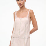 The Greta Dress is an elegant, sleeveless light pink midi dress with a square neckline and rows of small, iridescent buttons, perfect for evening dressing.