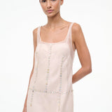 The Greta Dress is an elegant, sleeveless light pink midi dress with a square neckline and rows of small, iridescent buttons, perfect for evening dressing.