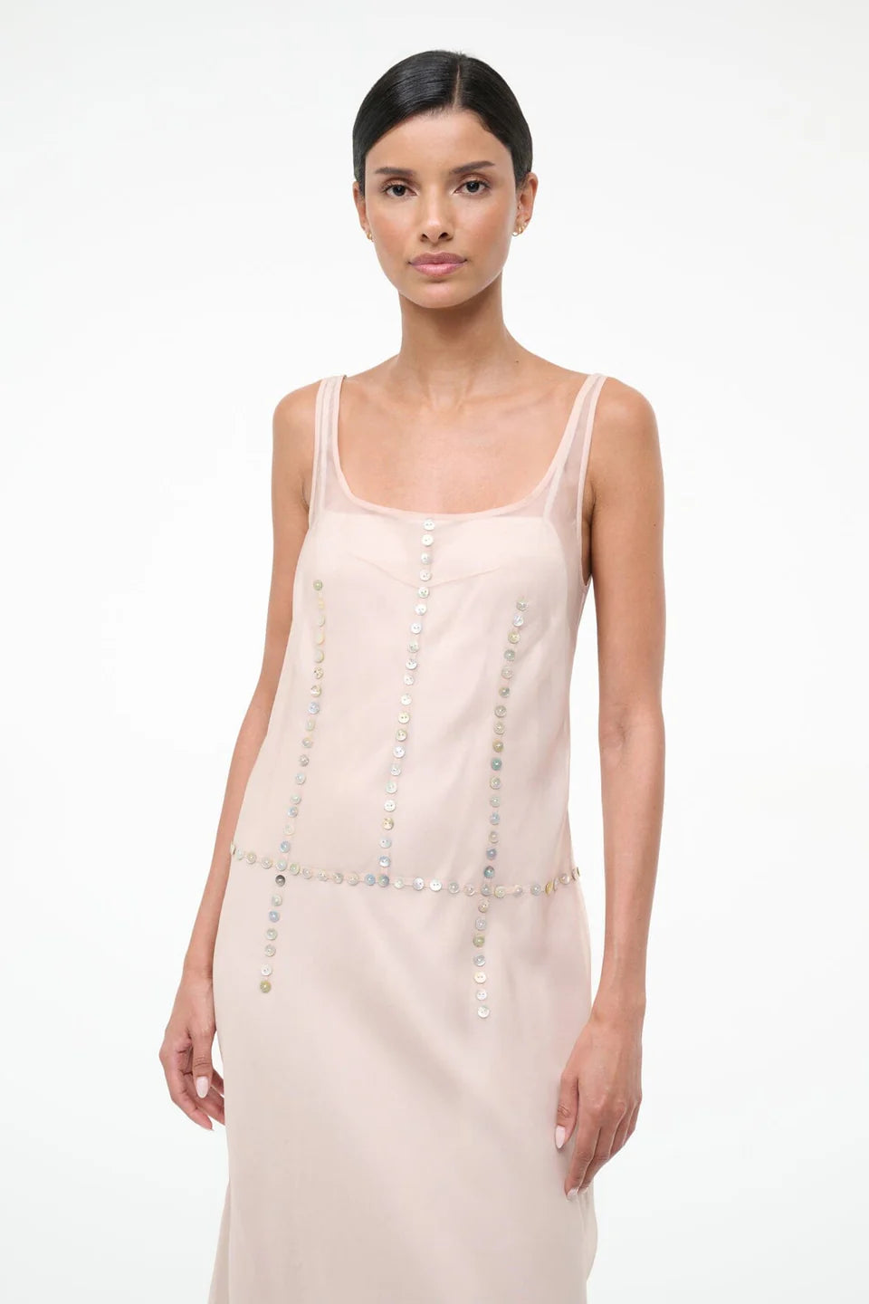 The Greta Dress is an elegant pale pink sleeveless dress with a scoop neckline and vertical and horizontal rows of small, iridescent buttons, perfect for evening dressing.