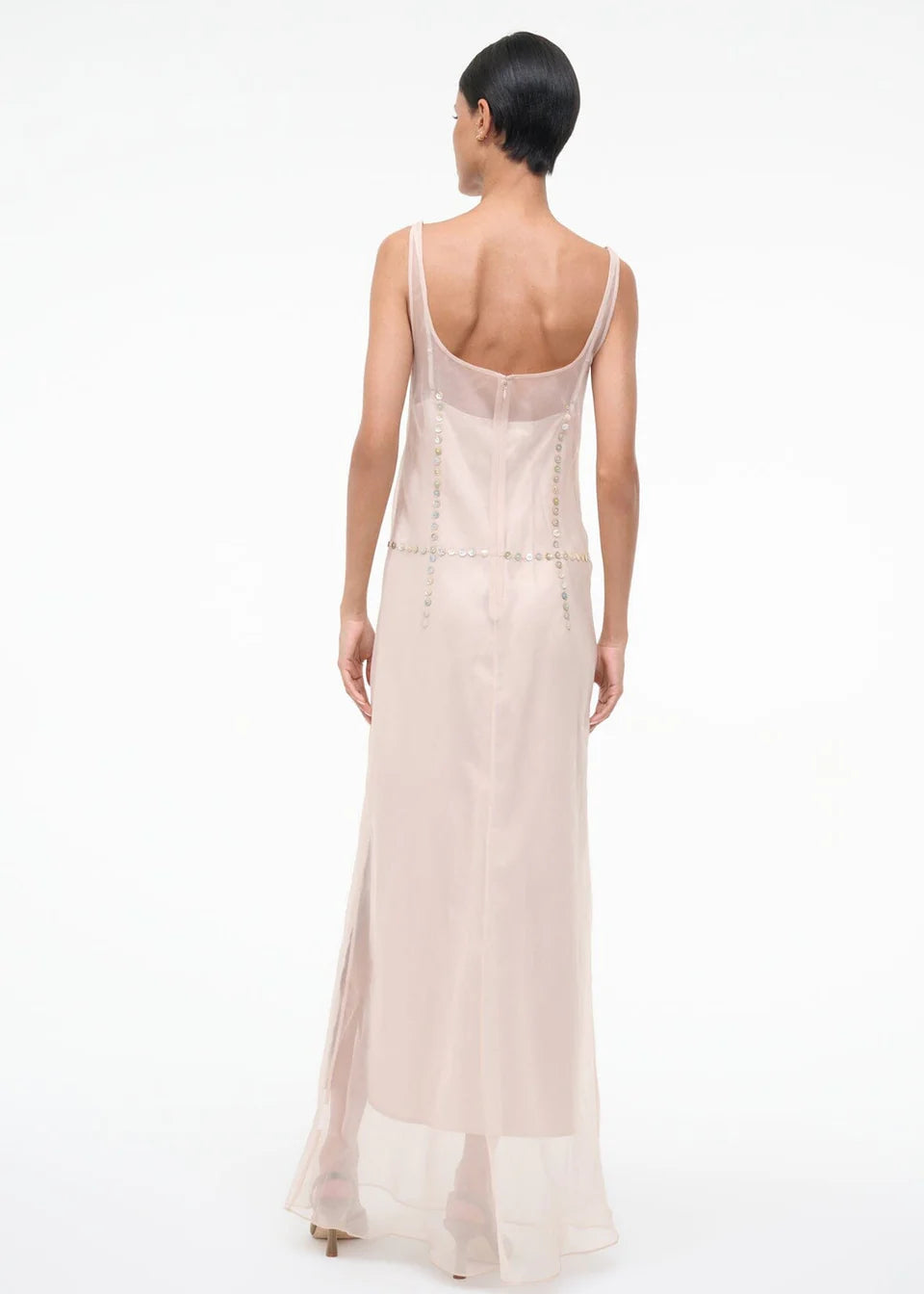 Back view of the Greta Dress, a pale pink sheer maxi dress for special occasions featuring a sleeveless silhouette, scoop back, and metallic disc embellishments at the waist.