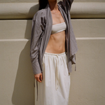 KABE SHOP INC Rhea maxi skirt in cream with an adjustable drawstring waistband, worn by a model against a wall.