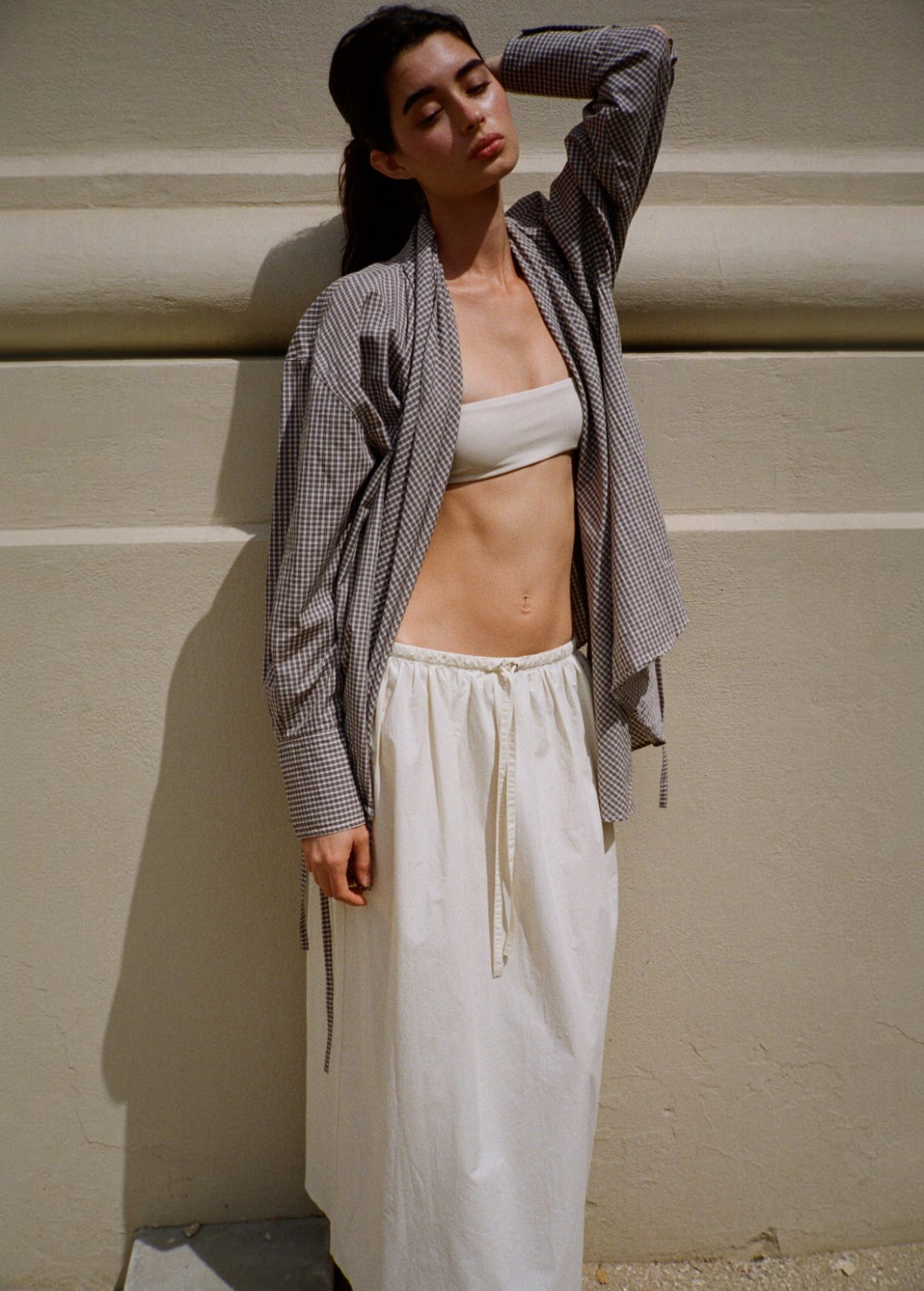 KABE SHOP INC Rhea maxi skirt in cream with an adjustable drawstring waistband, worn by a model against a wall.
