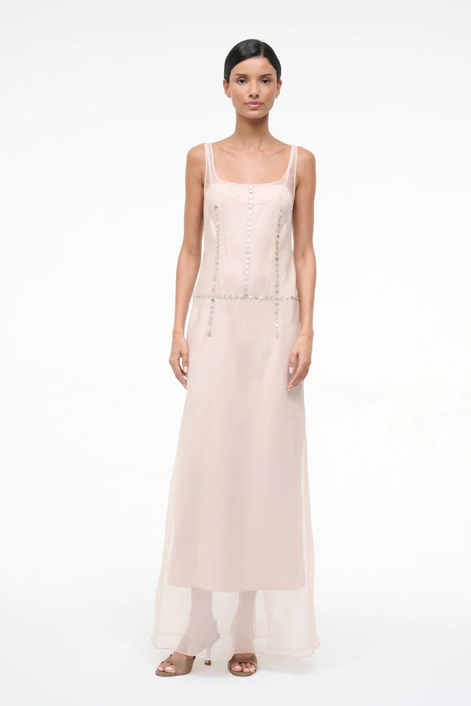 The Greta Dress is an elegant, floor-length, pale pink sleeveless evening dress featuring a scoop neckline and vertical rows of small decorative buttons.
