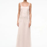 The Greta Dress is an elegant, floor-length, pale pink sleeveless evening dress featuring a scoop neckline and vertical rows of small decorative buttons.