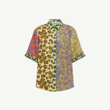 Patty Shirt, a short-sleeved button-up featuring a patchwork of floral prints in orange, brown, green, and purple, with ruffled cuffs for a contemporary touch.