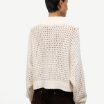 Back view of a person wearing a cream-colored, open-knit Cropped Hampton Sweater featuring a mock neck and ribbed hem.
