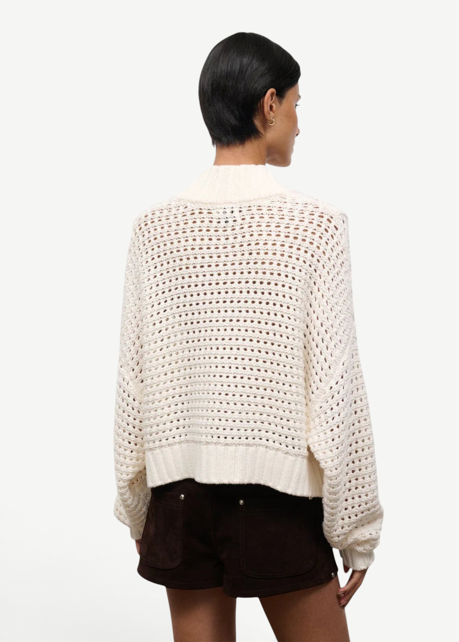 Back view of a person wearing a cream-colored, open-knit Cropped Hampton Sweater featuring a mock neck and ribbed hem.