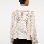 Back view of a person wearing a cream-colored, open-knit Cropped Hampton Sweater featuring a mock neck and ribbed hem.
