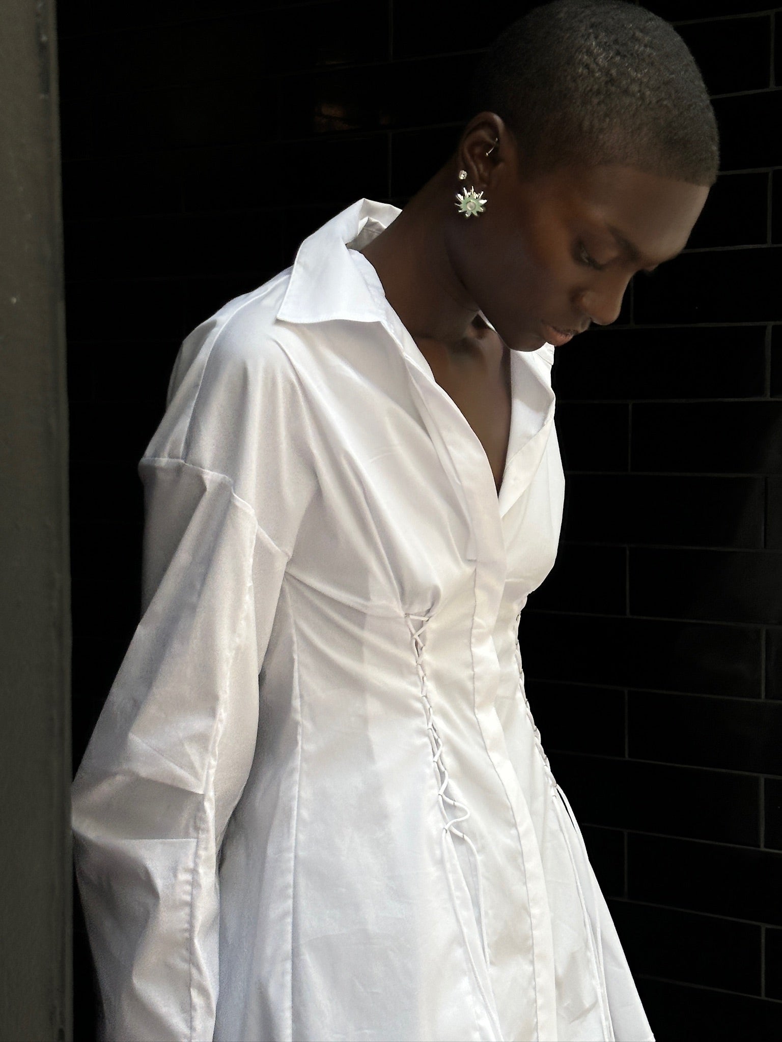 A person wears a white long-sleeved Laced Button Down shirt featuring side corset-style lace-up detailing for a feminine silhouette.