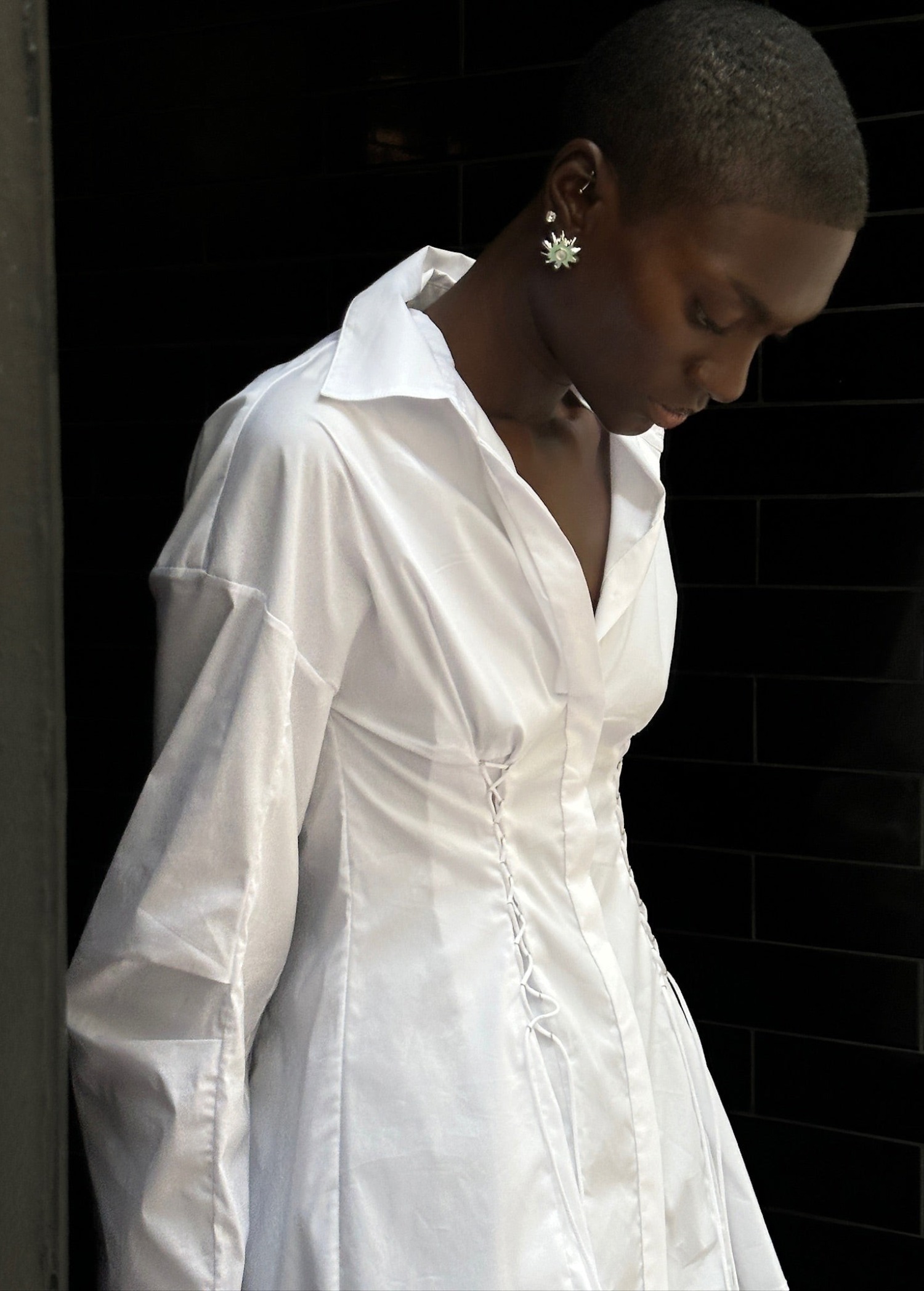 A person wears a white long-sleeved Laced Button Down shirt featuring side corset-style lace-up detailing for a feminine silhouette.