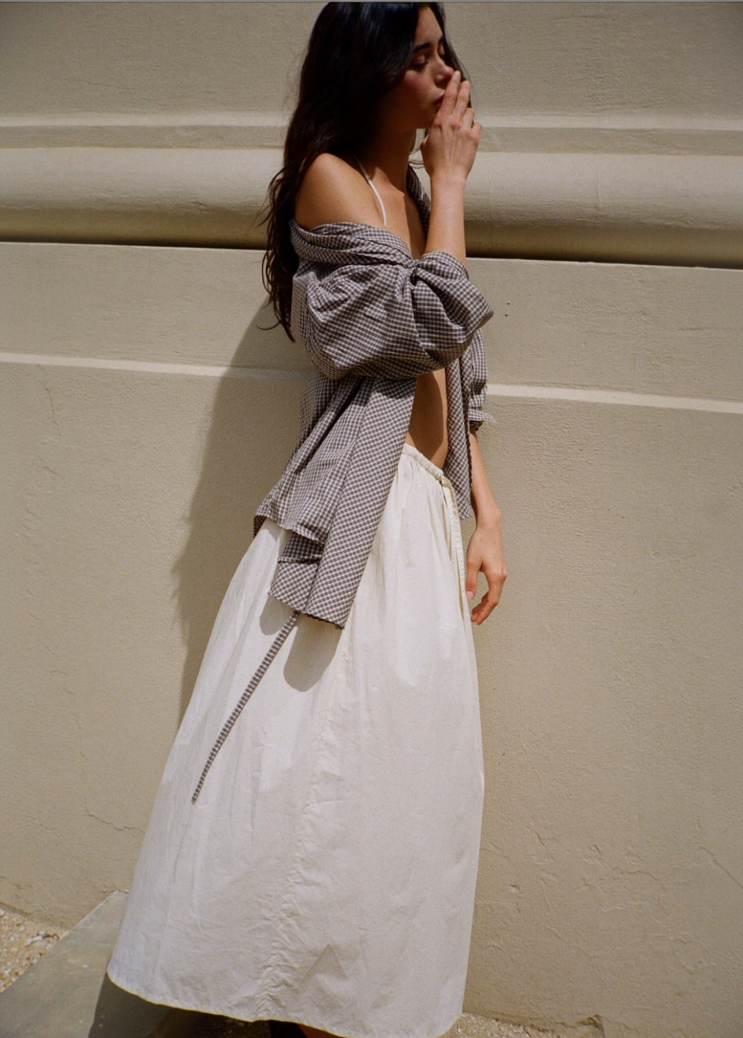 KABE SHOP INC Rhea maxi skirt in cream with an adjustable waistband, styled with a gingham shirt against a wall.