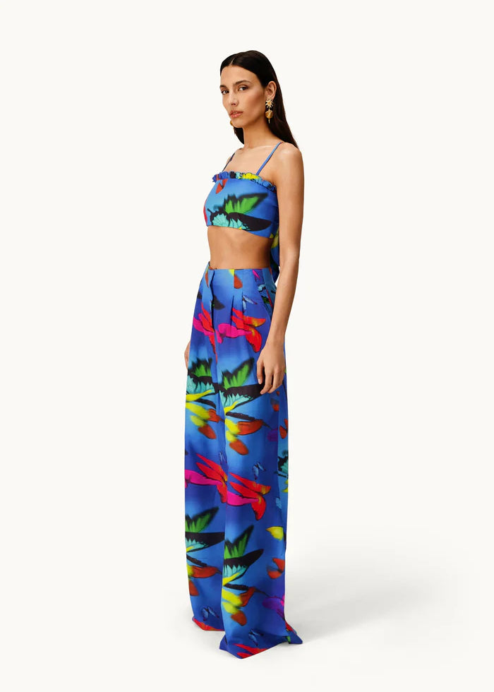 Woman wearing the Alma Set—a colorful blue linen crop top and wide-leg pants ensemble featuring a vibrant abstract floral pattern—standing against a light background, perfect for versatile styling with adaptable accessories.
