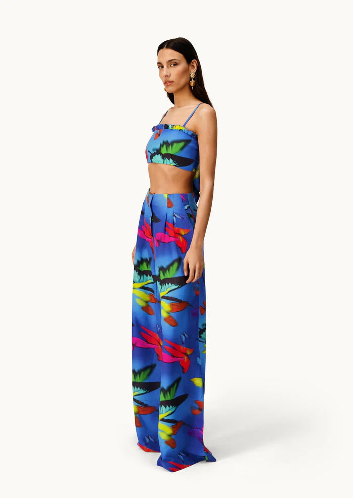 Woman wearing the Alma Set—a colorful blue linen crop top and wide-leg pants ensemble featuring a vibrant abstract floral pattern—standing against a light background, perfect for versatile styling with adaptable accessories.