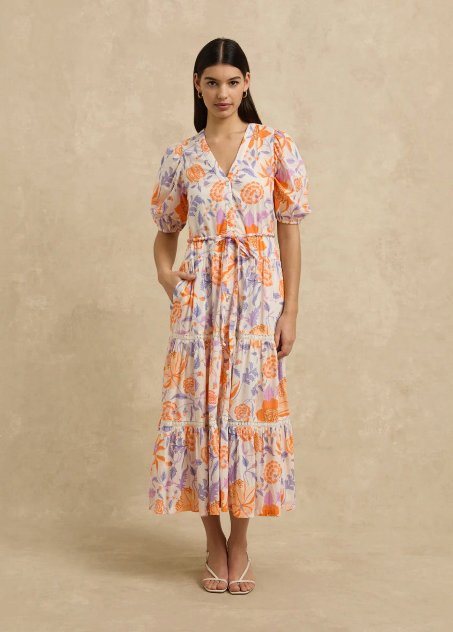 Model wearing KABE SHOP INC Anyeta Dress in cream with orange and purple floral print, puff sleeves, and midi length.