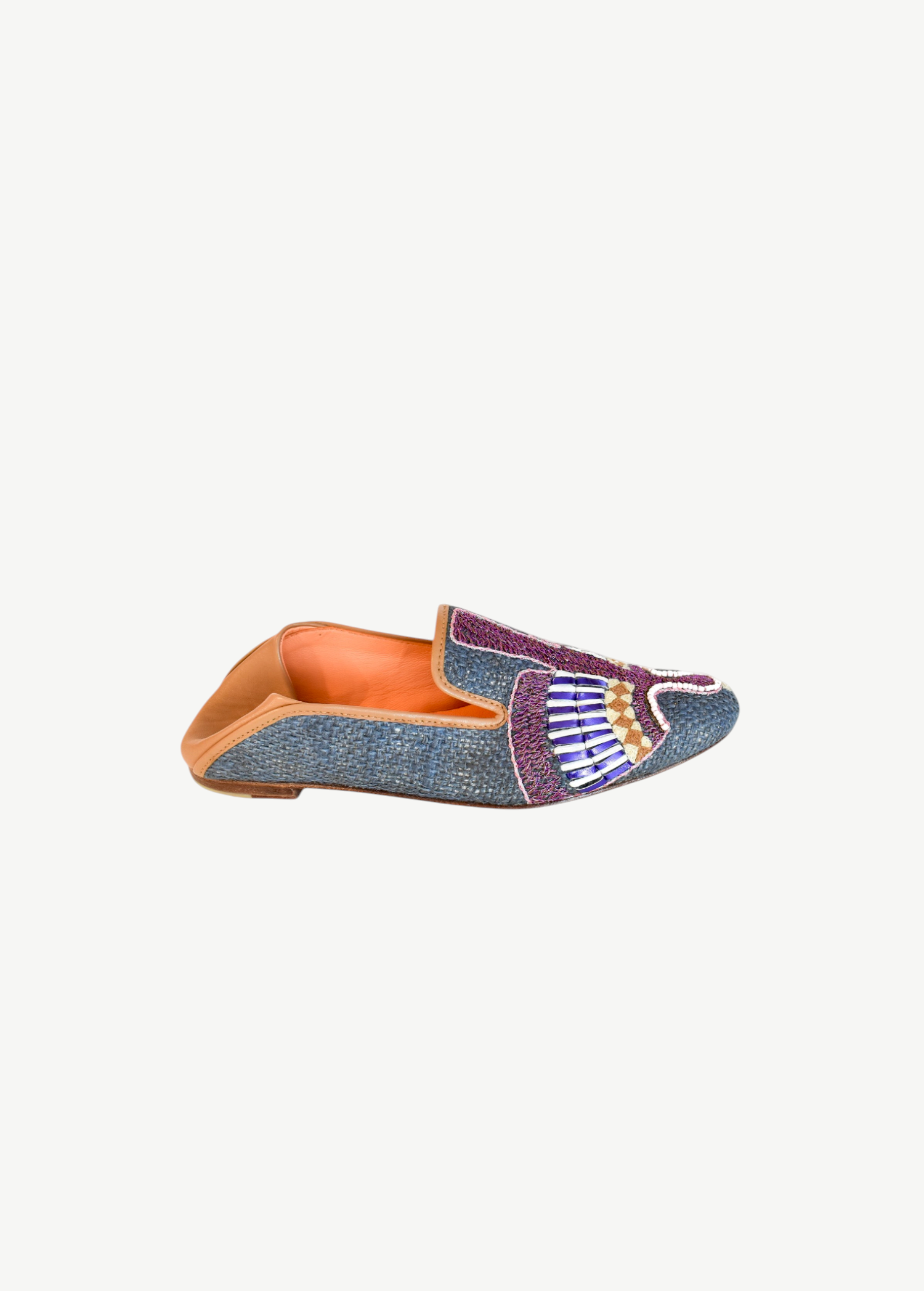 Introducing the Anzu Moccasin—a blue woven loafer with tan leather lining and sole, showcasing intricate purple, white, gold, and blue beaded embroidery on the upper. This hand-embroidered leather moccasin is perfect for making a stylish statement.
