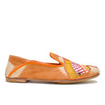 The Anzu Moccasin is a brown and beige slip-on flat shoe with orange trim, showcasing a vibrant hand-embroidered moccasin design highlighted by yellow, pink, and gold accents on the side.