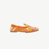 The Anzu Moccasin is a brown and beige slip-on flat shoe with orange trim, showcasing a vibrant hand-embroidered moccasin design highlighted by yellow, pink, and gold accents on the side.