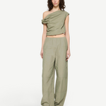 A model wears the Alice Top, a sage green, contemporary off-the-shoulder draped crop top, with matching high-waisted wide-leg trousers.