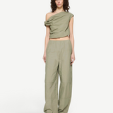 A model wears the Alice Top, a sage green, contemporary off-the-shoulder draped crop top, with matching high-waisted wide-leg trousers.