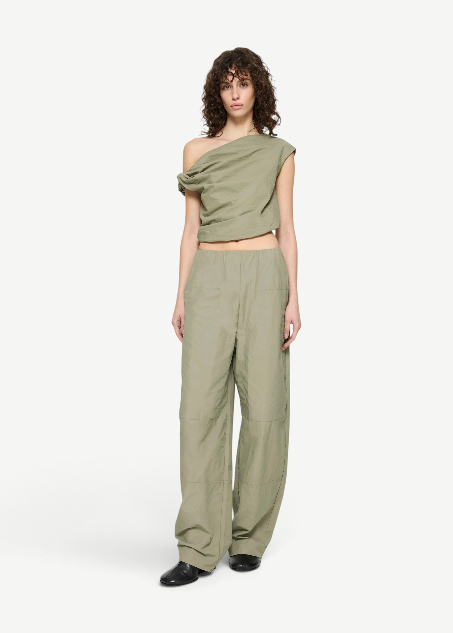 A model wears the Alice Top, a sage green, contemporary off-the-shoulder draped crop top, with matching high-waisted wide-leg trousers.