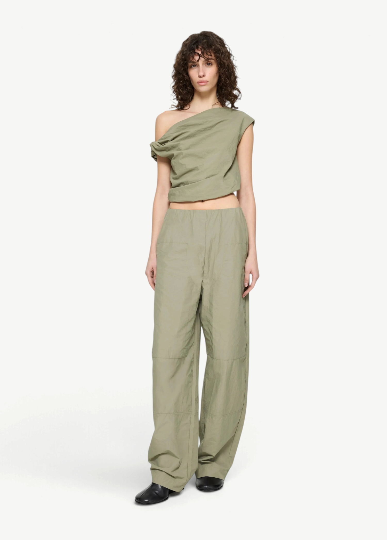 A model wears the Alice Top, a sage green, contemporary off-the-shoulder draped crop top, with matching high-waisted wide-leg trousers.