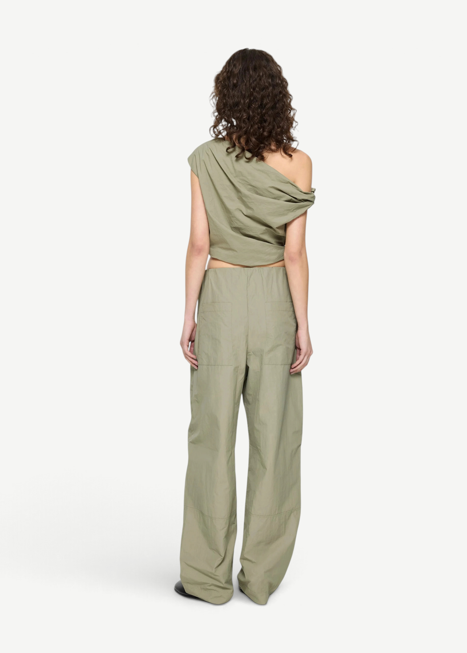 Back view of a person wearing a sage green asymmetric, sculptural Alice Top and matching wide-leg trousers.