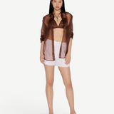 Model wearing KABE SHOP INC Kira white shorts with scalloped hem, paired with a brown sheer shirt and beige mules.