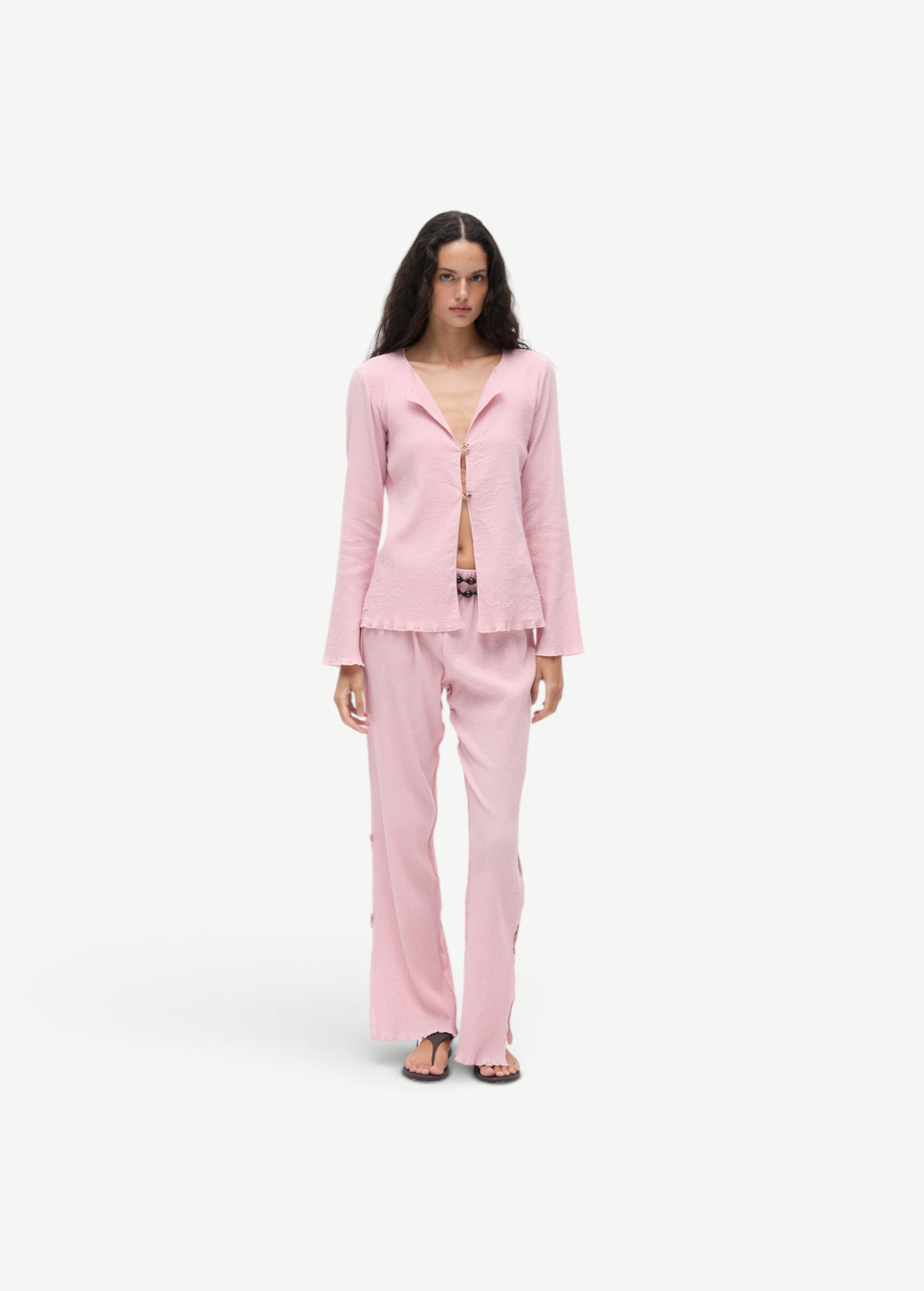 Model wearing KABE SHOP INC Malaika pants in light pink with a matching textured long-sleeve button-up shirt