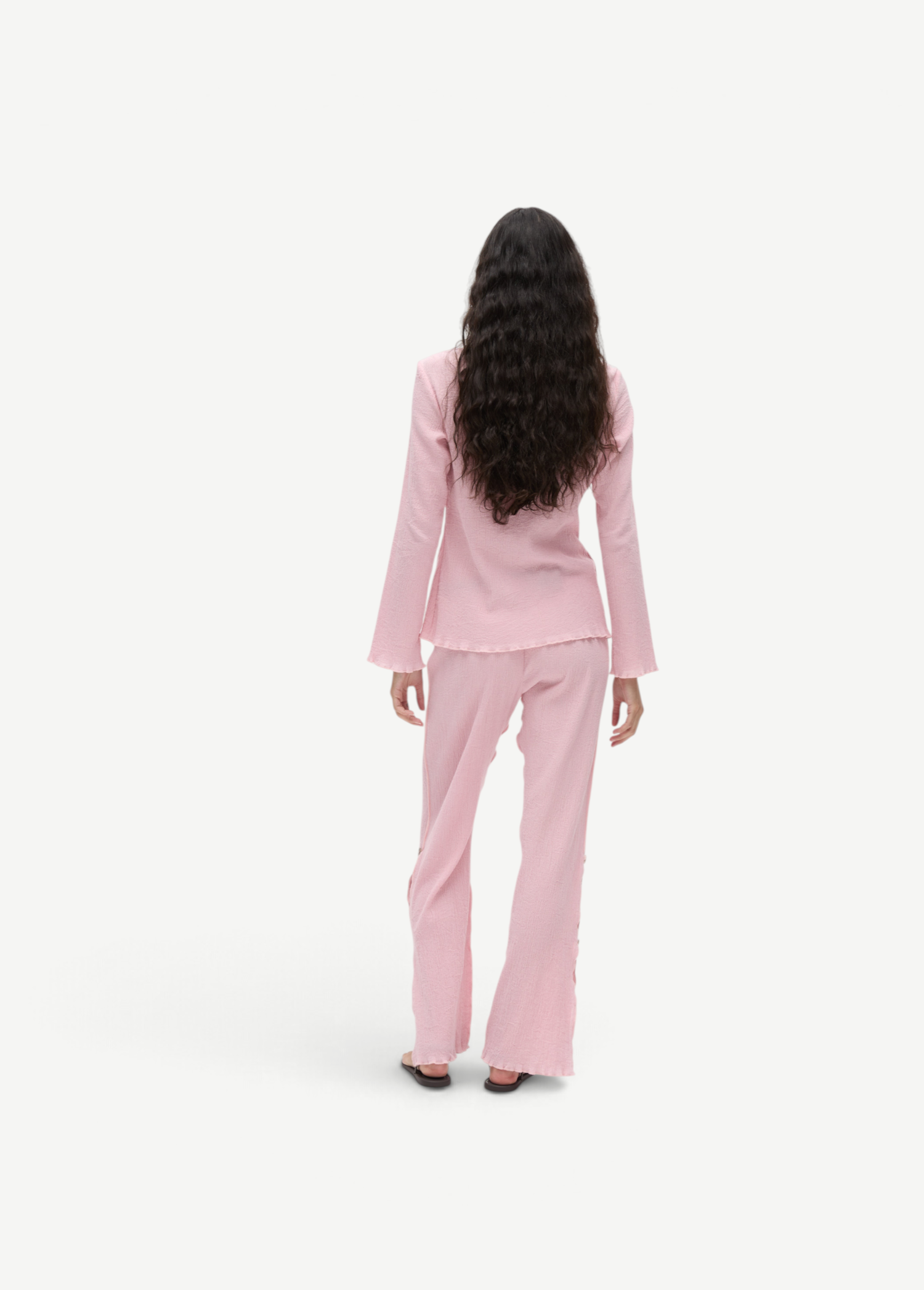 Back view of a woman wearing KABE SHOP INC Malaika Pants in a light pink textured fabric with a straight-leg fit.