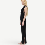Model wearing KABE SHOP INC Malaika black straight-leg pants with side slit and button detail, side profile view.