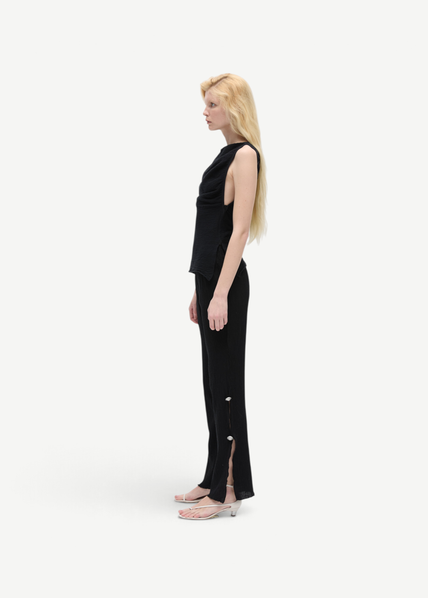 Model wearing KABE SHOP INC Malaika black straight-leg pants with side slit and button detail, side profile view.
