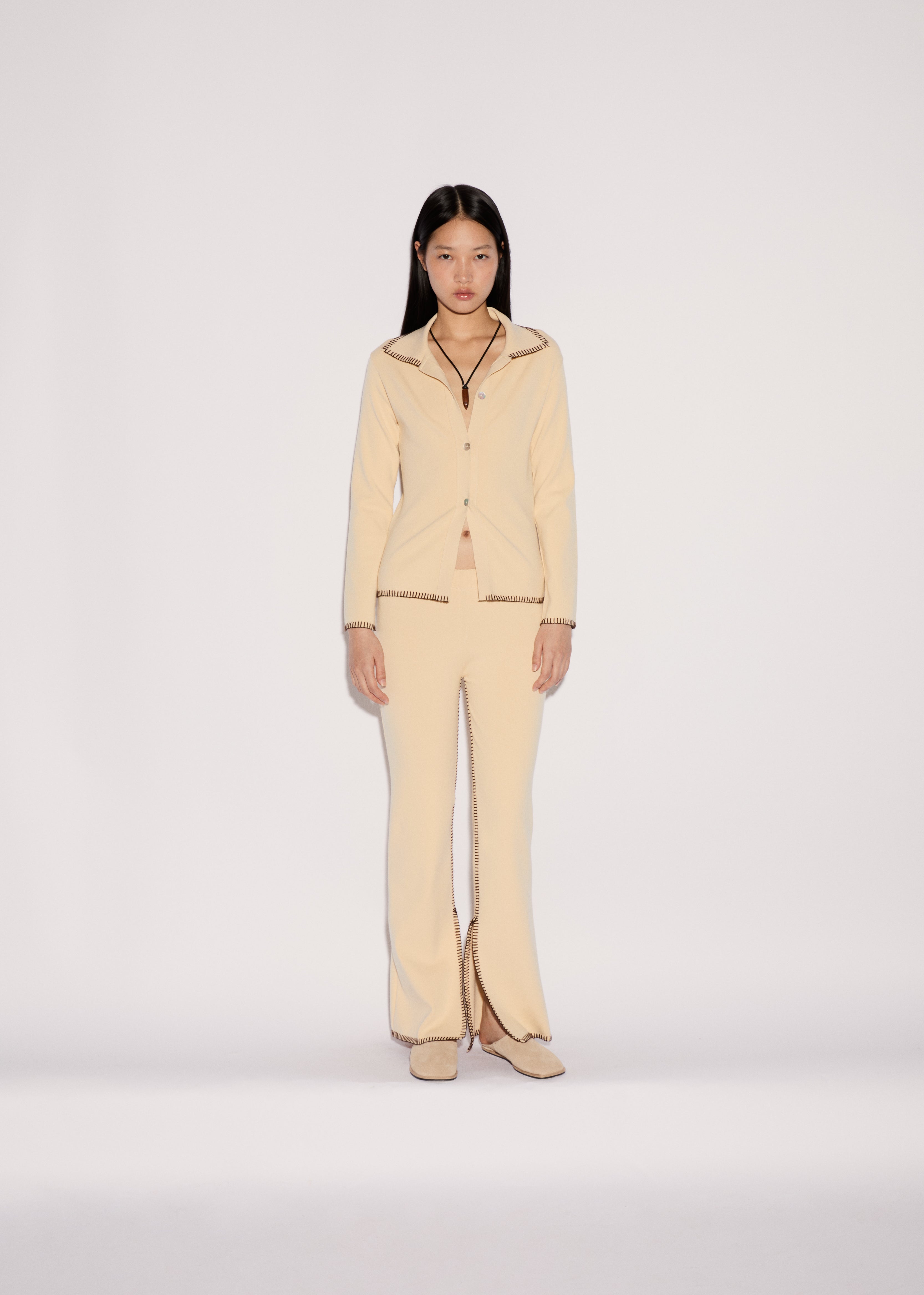 A model wears the light yellow Iris Top and matching flared trousers featuring a relaxed silhouette and visible dark stitched edges.