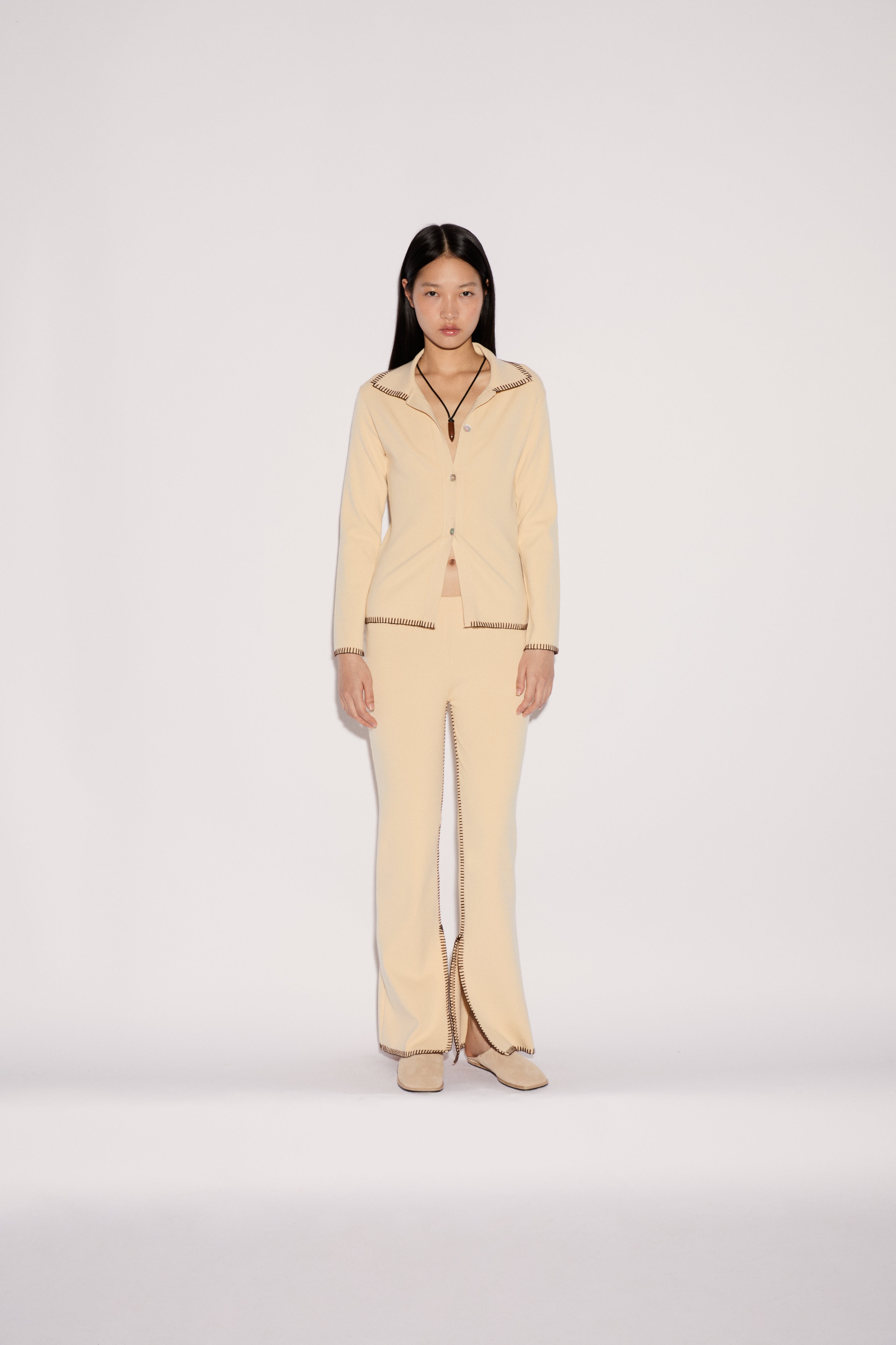 A model wears the light yellow Iris Top and matching flared trousers featuring a relaxed silhouette and visible dark stitched edges.