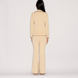Back view of a person in a relaxed silhouette wearing a cream-colored Iris Top and matching flared trousers, both finished with decorative brown whipstitching along the hems and edges.
