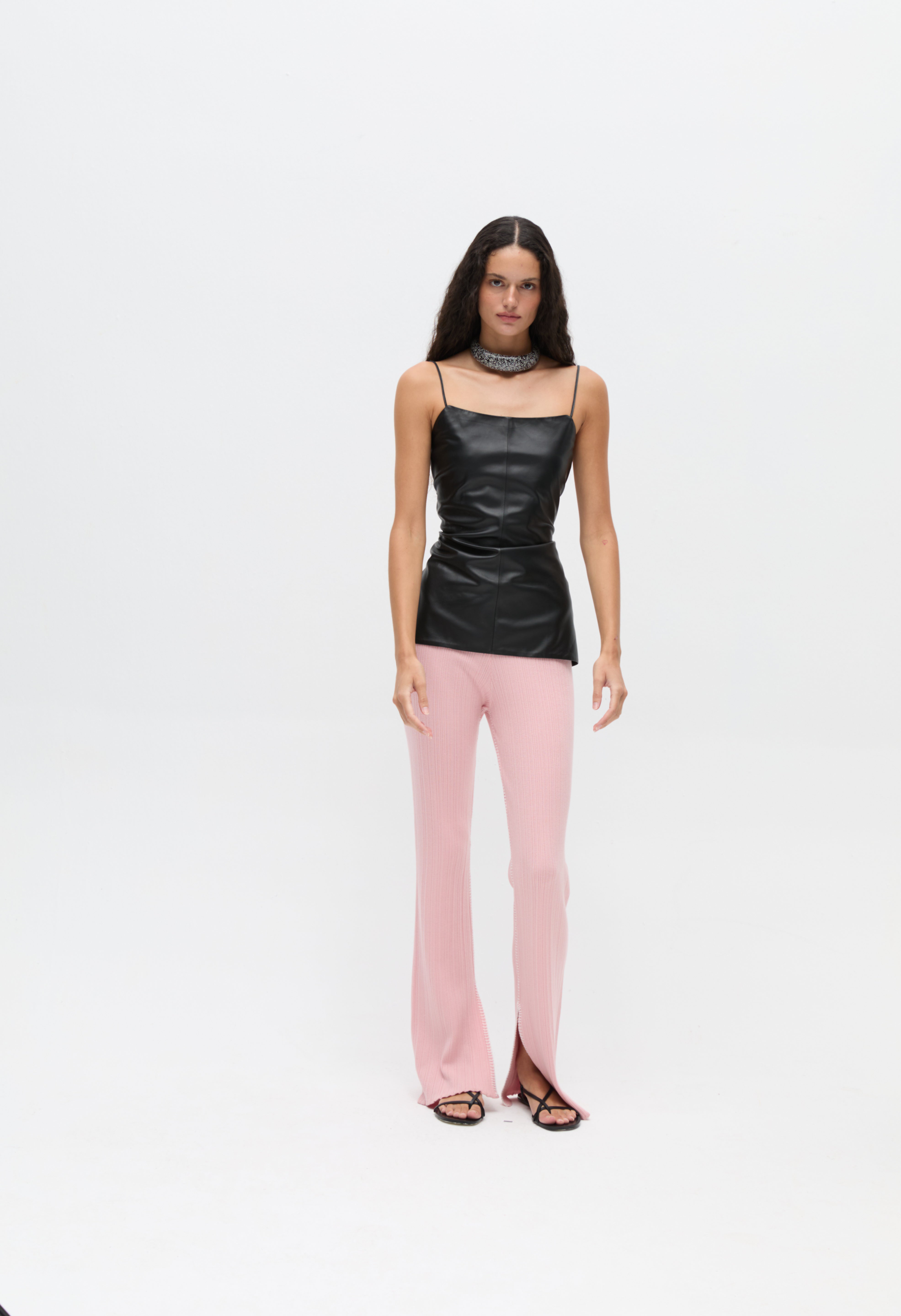 A model wears a black spaghetti strap Xena Top with light pink ribbed flared trousers featuring hem slits, creating a body-hugging silhouette.