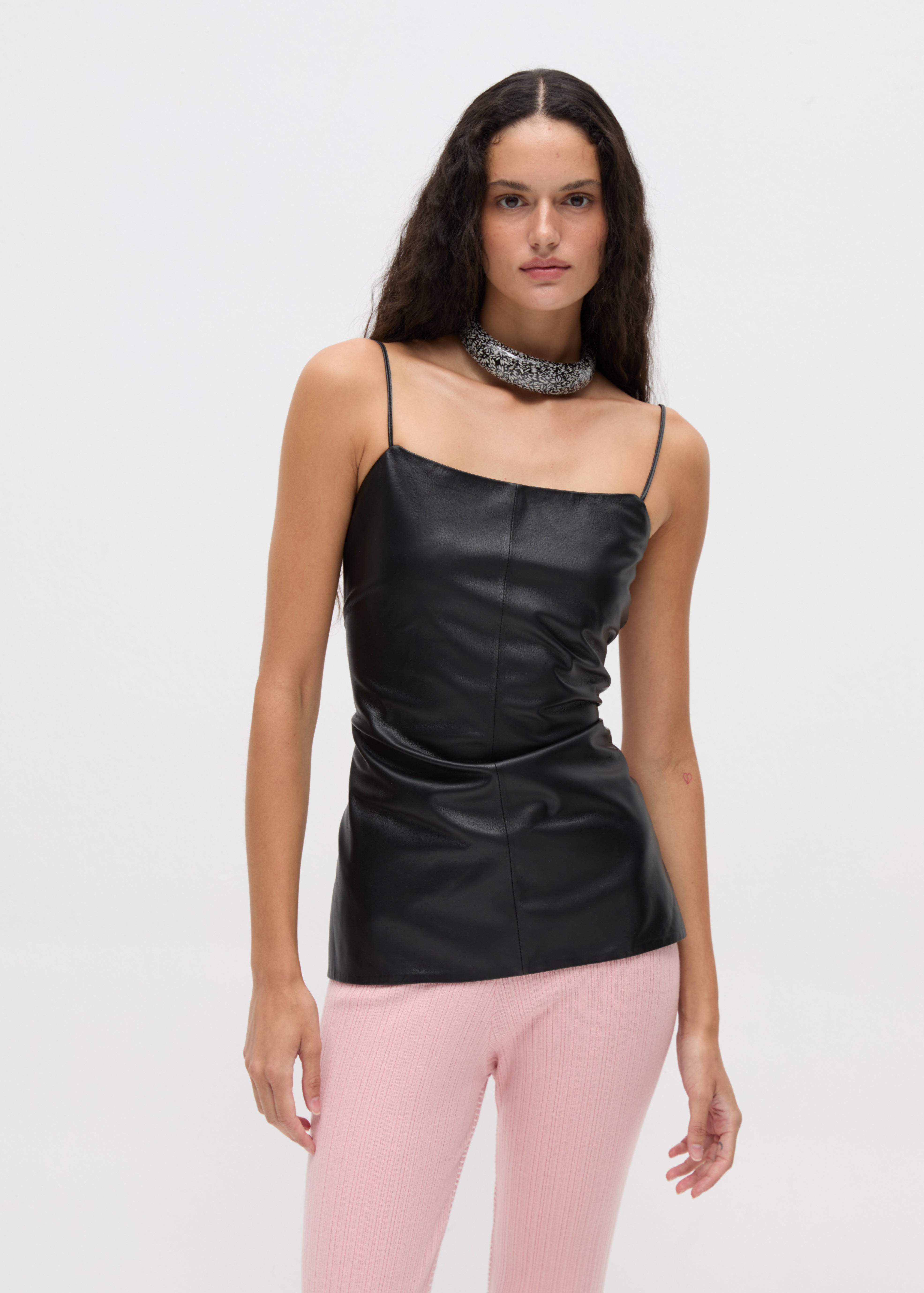 A person wearing a minimalist, body-hugging Xena Top in black faux-leather with thin straps and a wide, sparkling silver choker necklace.
