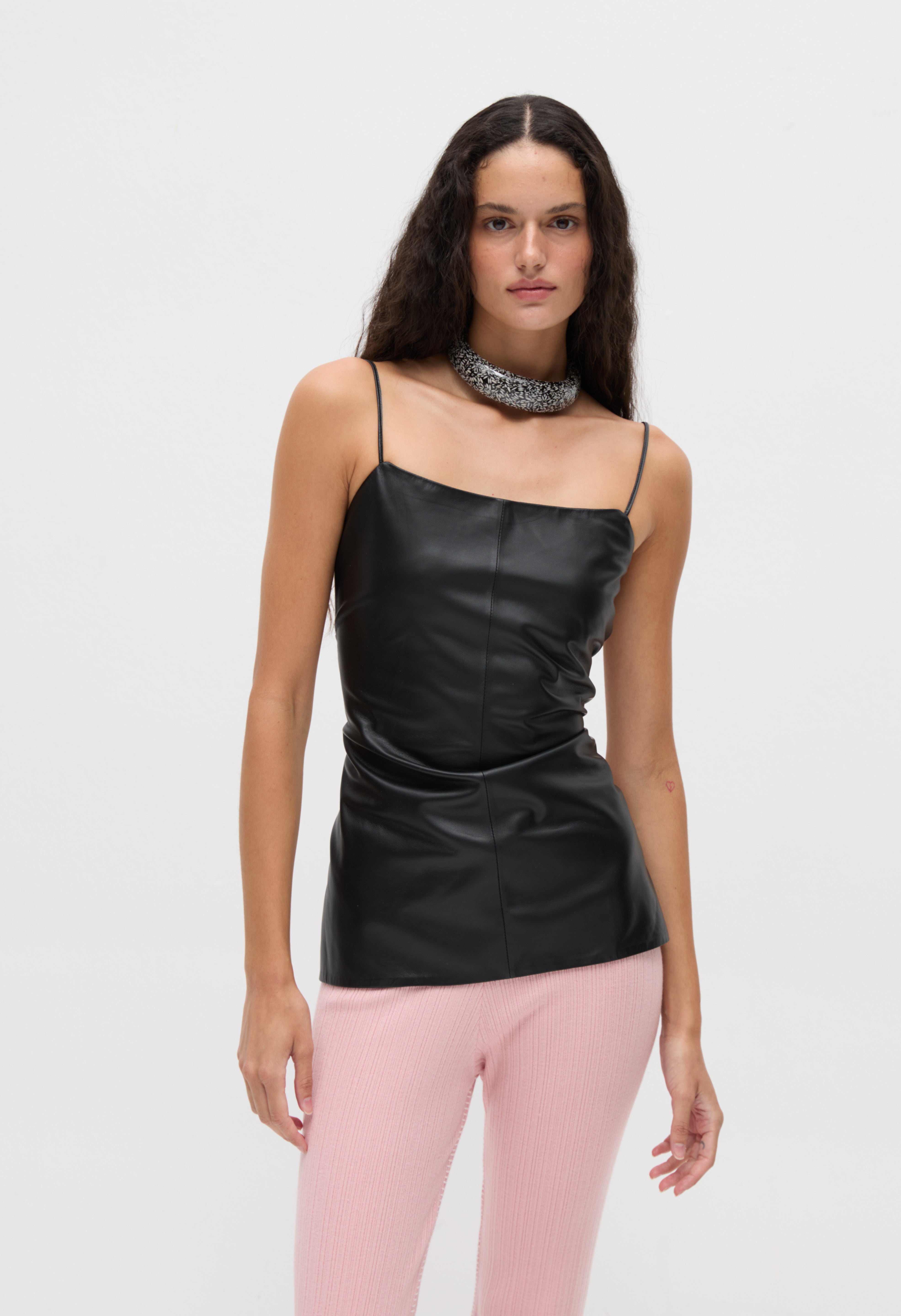 A person wearing a minimalist, body-hugging Xena Top in black faux-leather with thin straps and a wide, sparkling silver choker necklace.