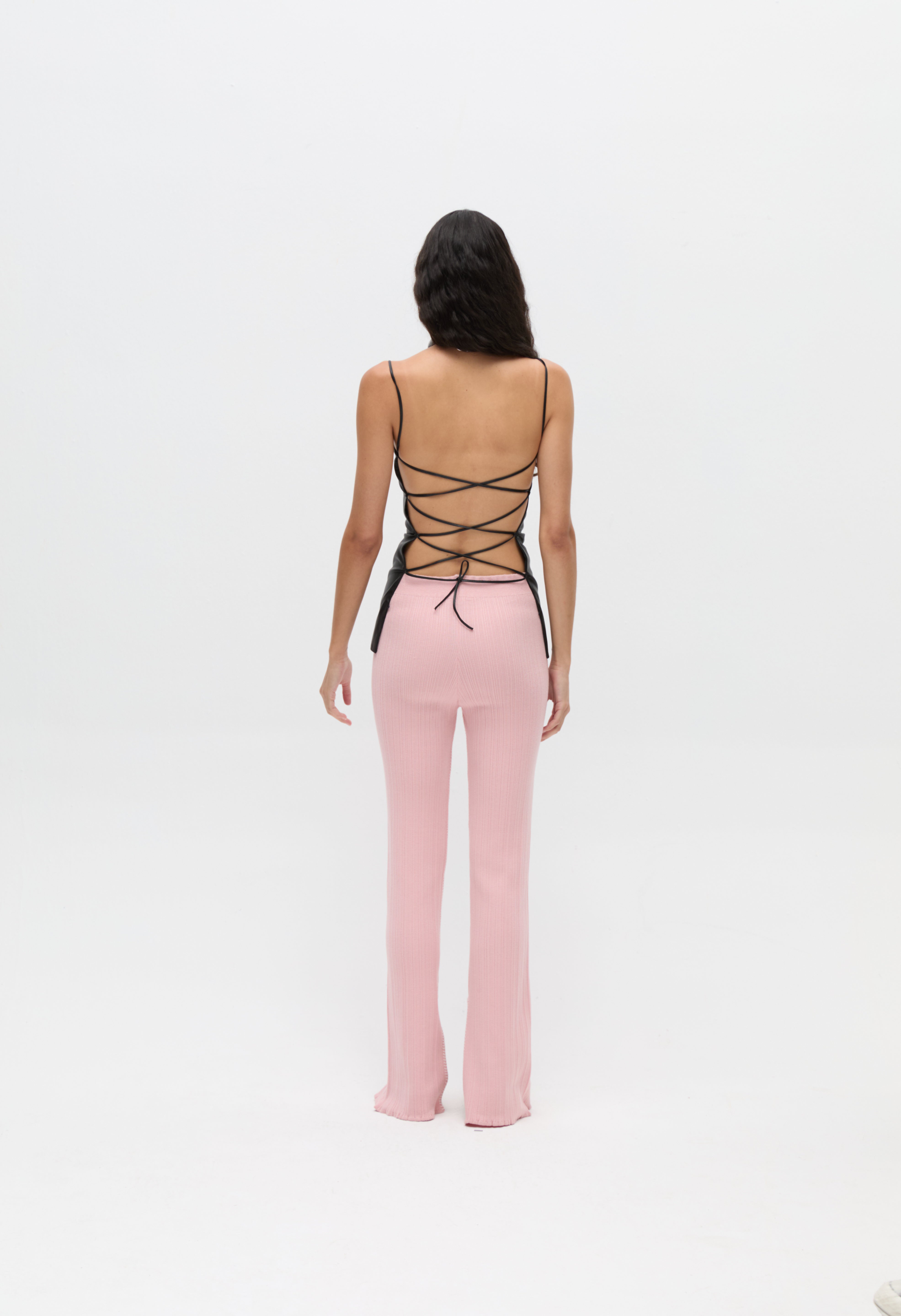 A body-hugging Xena Top with thin straps and a lace-up tie closure, paired with pink ribbed pants.